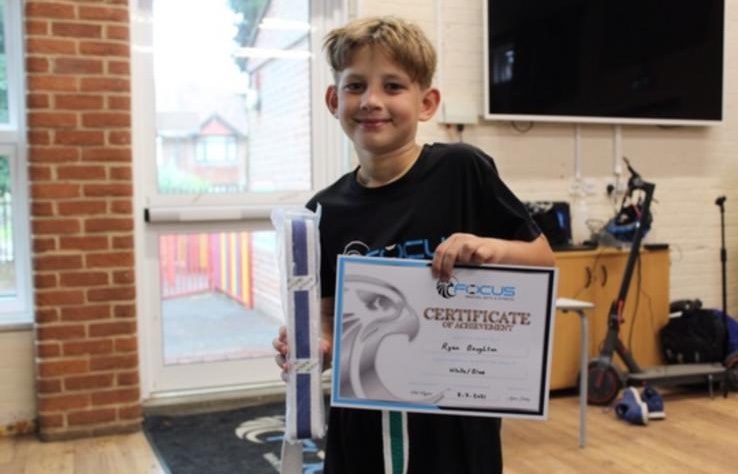 A young student holding his new belt and certificate of achievement