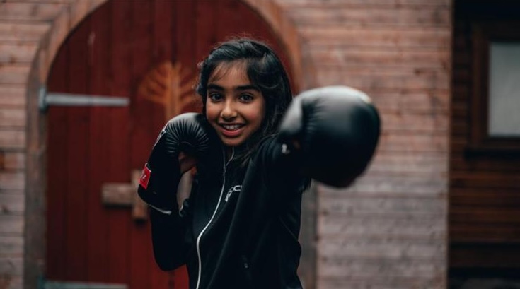 A young student smiling with her boxing gloves on
